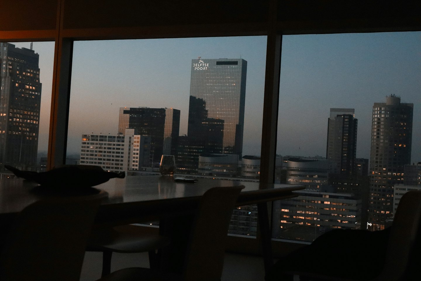 Stadsgezicht bij schemering gezien door een raam met silhouetten van tafels.